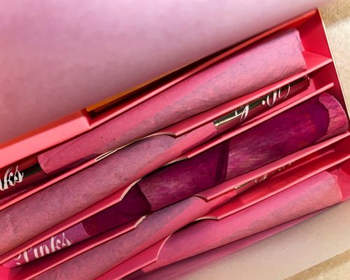 an open pack of glamorous pinks cannabis prerolls, with 4 prerolls wrapped in pink paper and 1 wrapped in rose petals