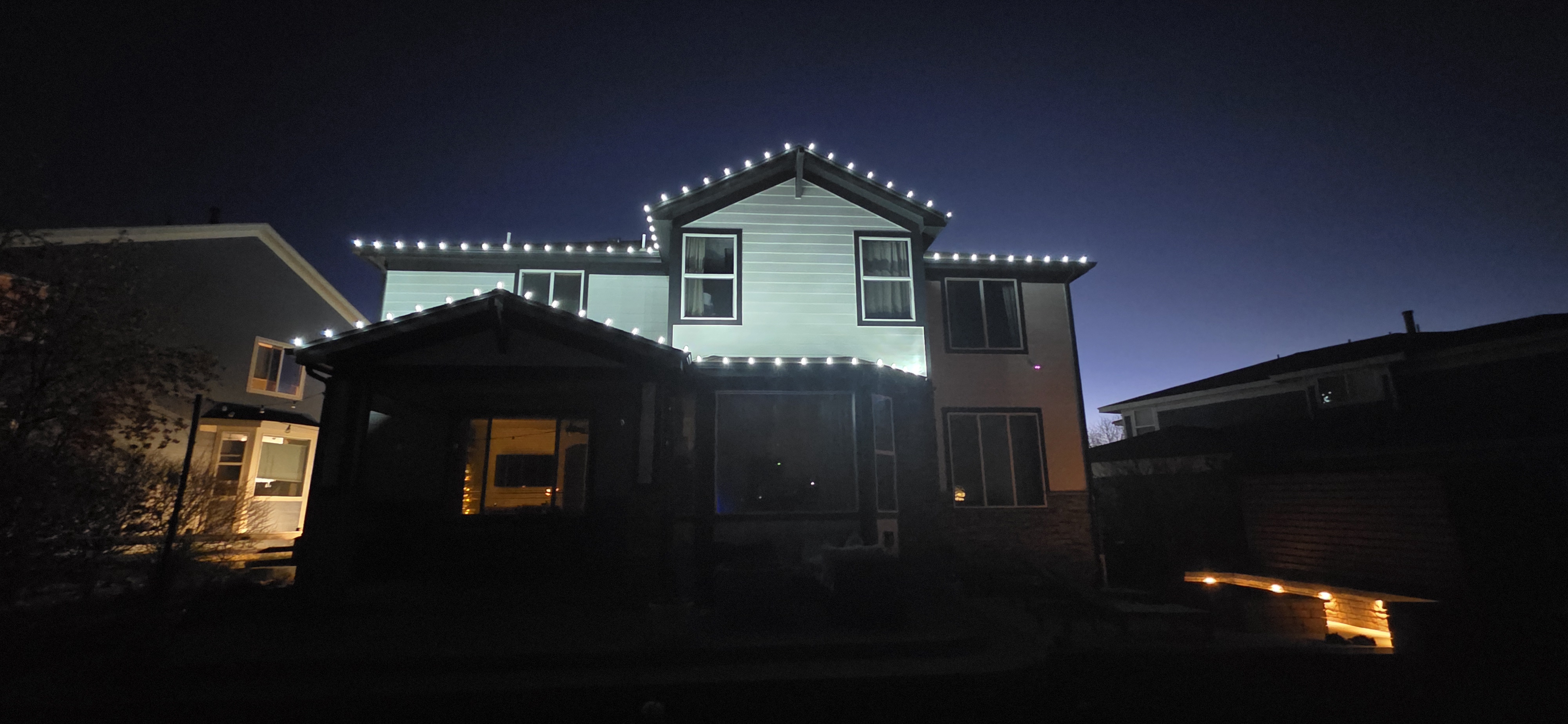 Professional white Christmas roofline lighting installed on a two-story Denver-area home