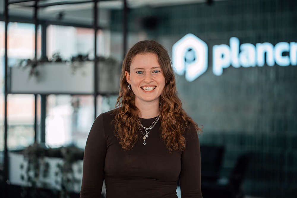 Portrait of Birte, Marketing Operations Manager, RevOps at plancraft, smiling in front of the plancraft office logo wall.