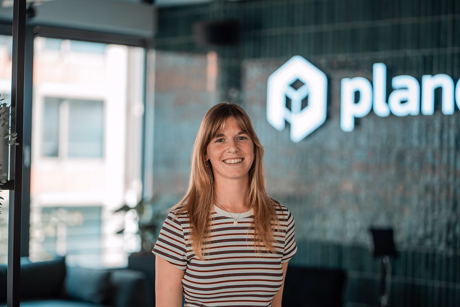 Portrait of Lies, Revenue Enablement Manager at plancraft, smiling in front of the plancraft office logo wall.