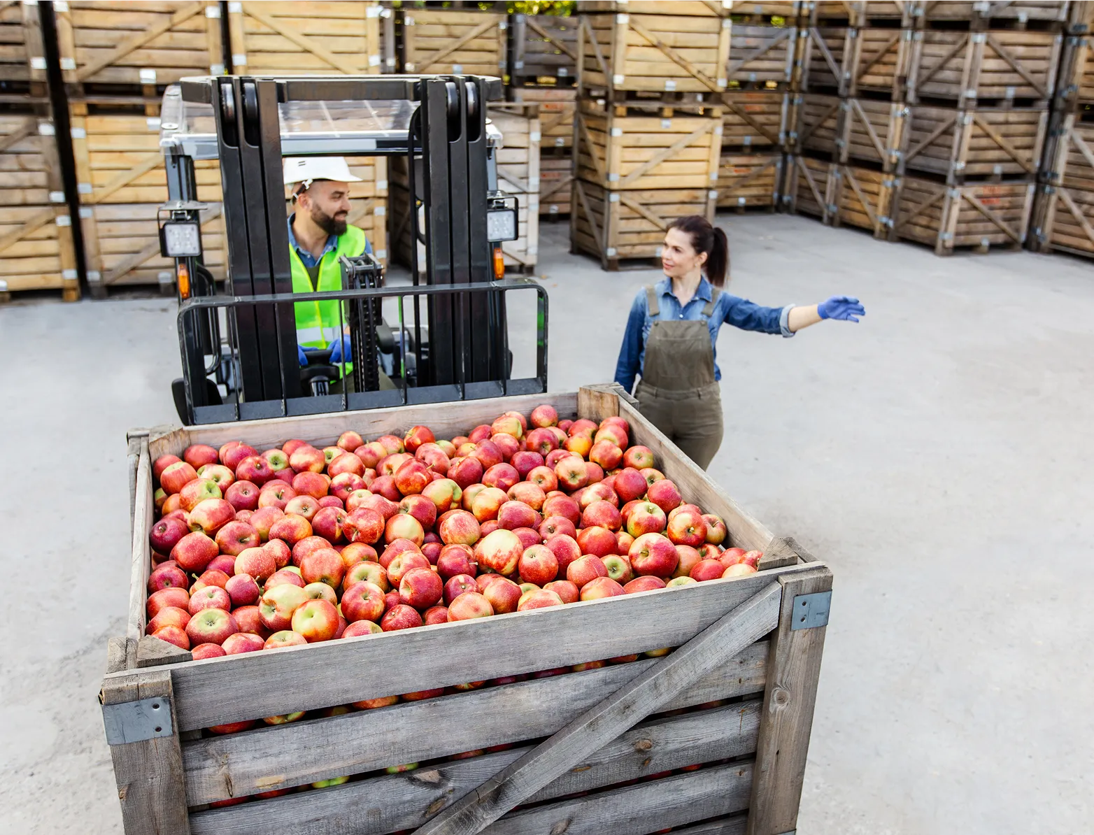 мъж и жена, работещи в склад, мъжът носи пале с ябълки на репатрак