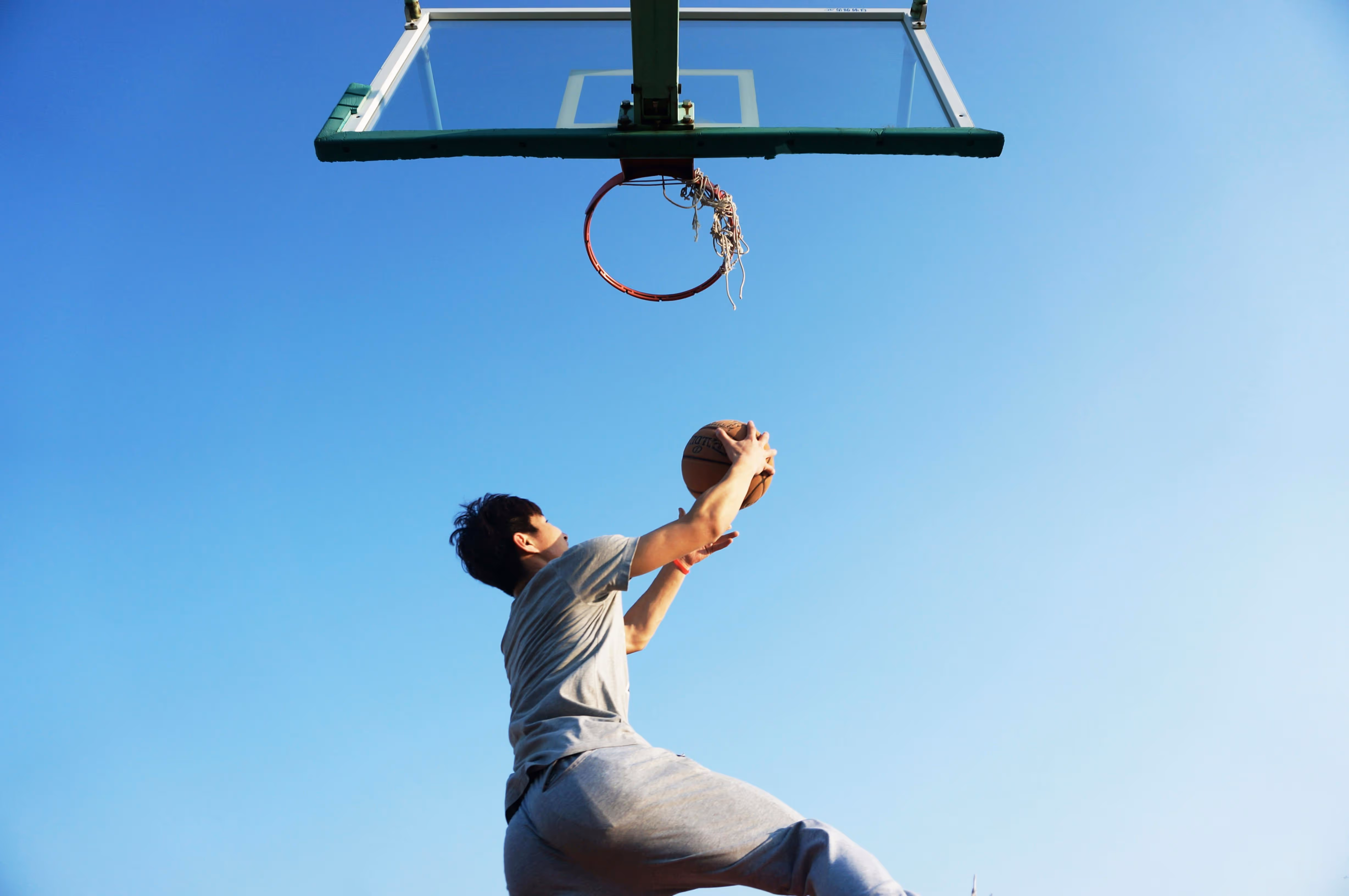 Eine Person wirft einen Basketball auf einen Freiplatzkorb unter blauem Himmel.