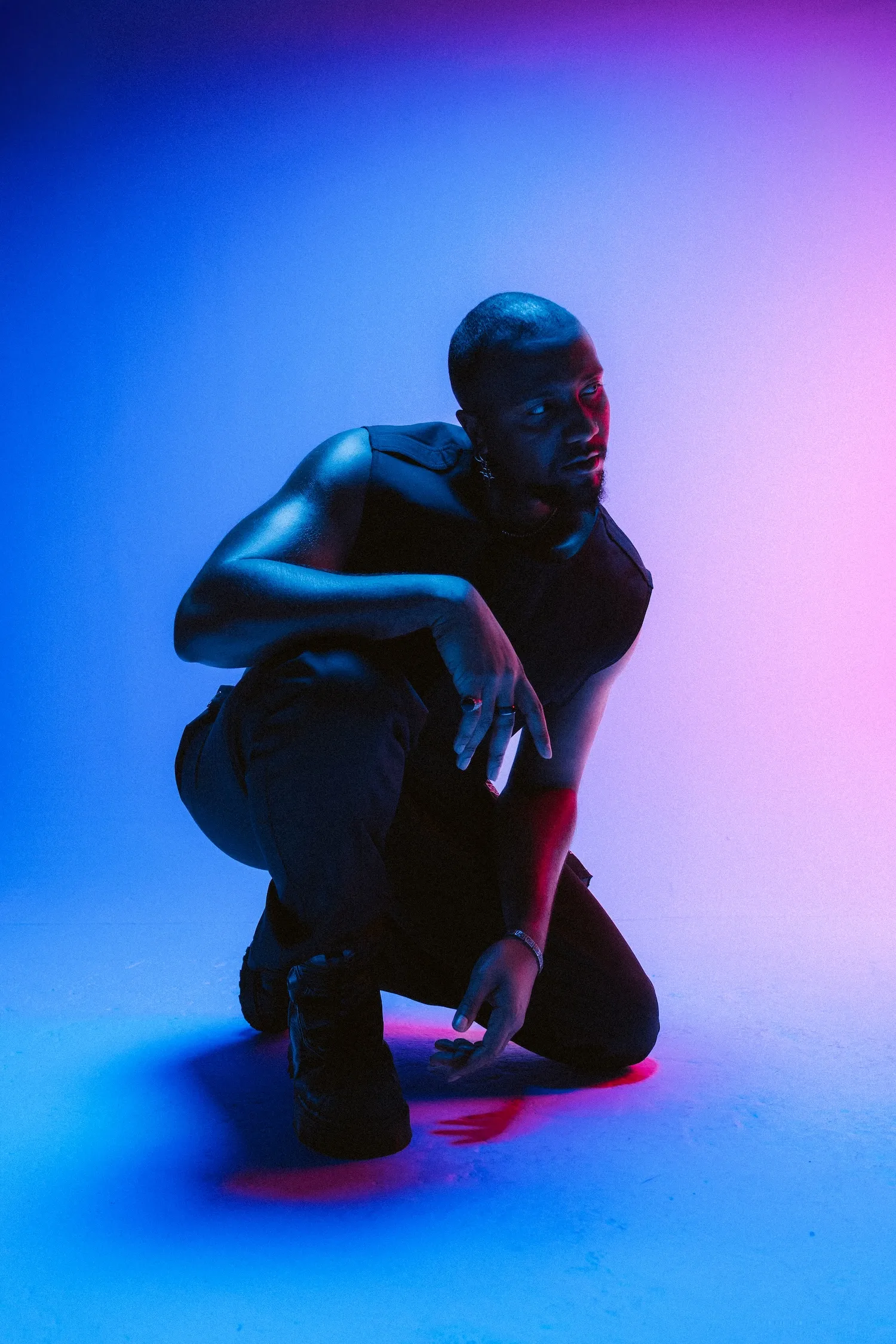 Person kneeling in contemplative pose with blue and pink neon lighting.
