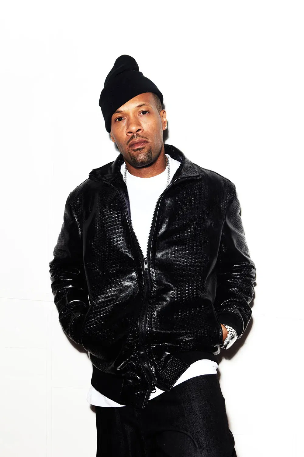 Man in black beanie and textured jacket poses against white background