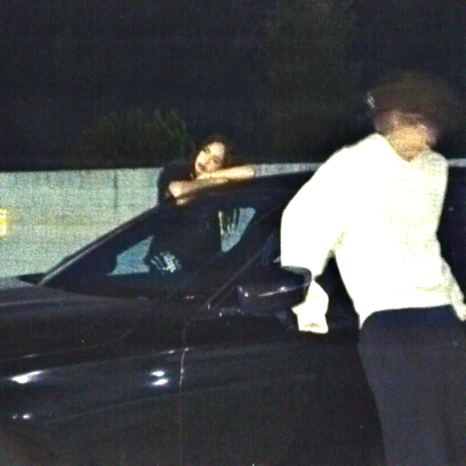 Grainy vintage footage of man in white shirt leaning into dark car window at night