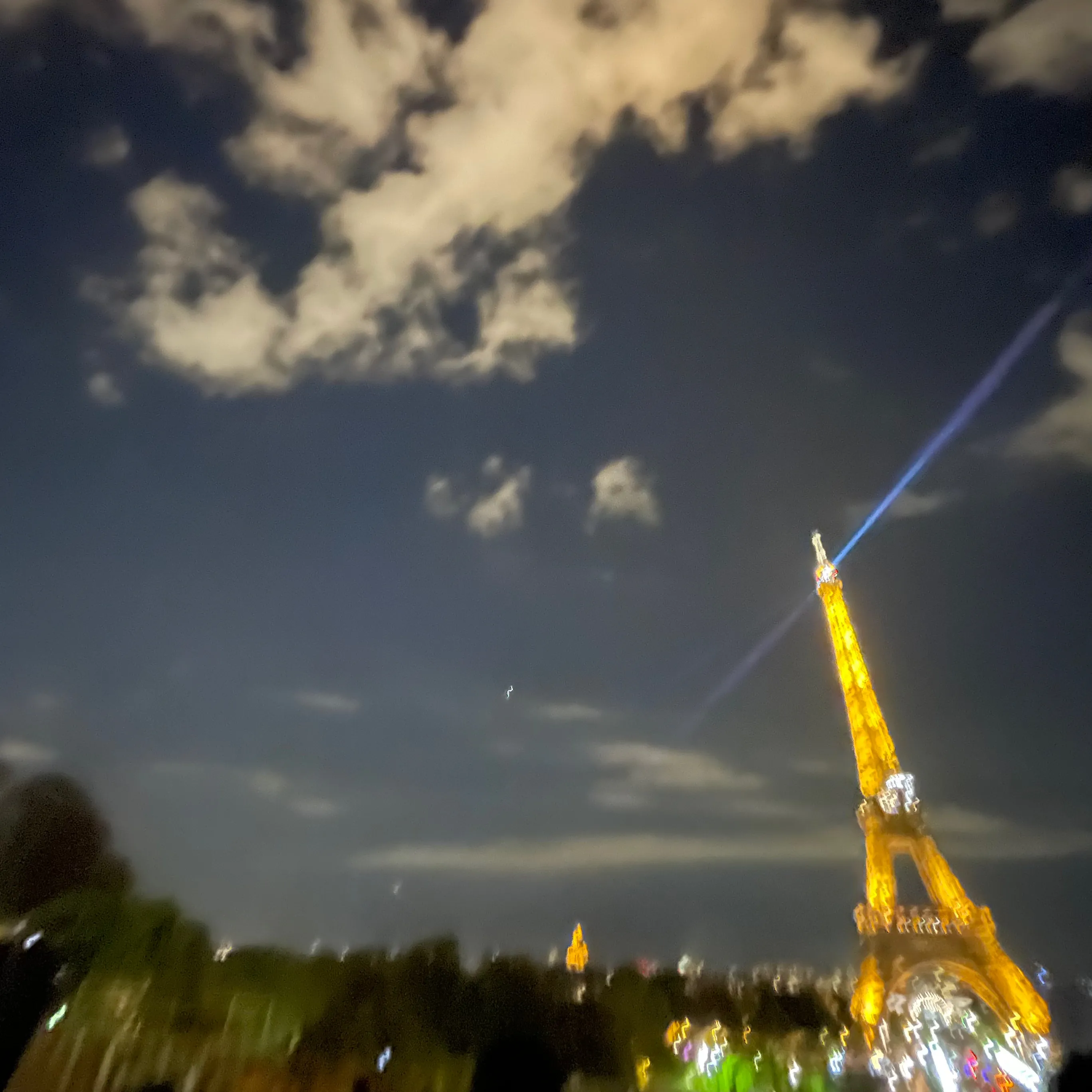 Illuminated Eiffel Tower at night with blue searchlight and cloudy sky background