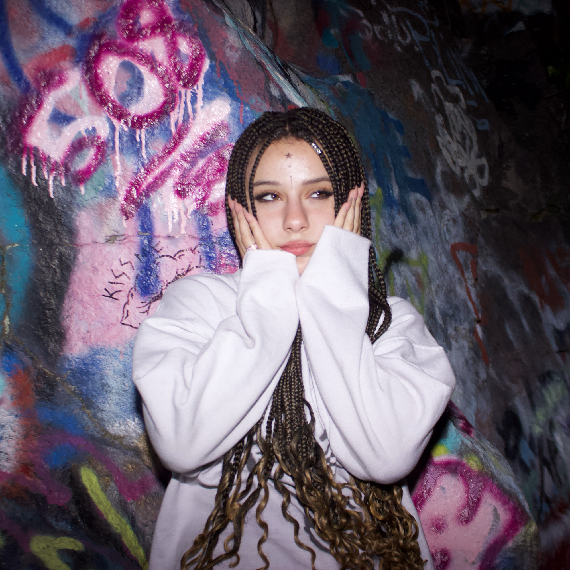 Woman with braids in white jacket posing against colorful graffiti wall.