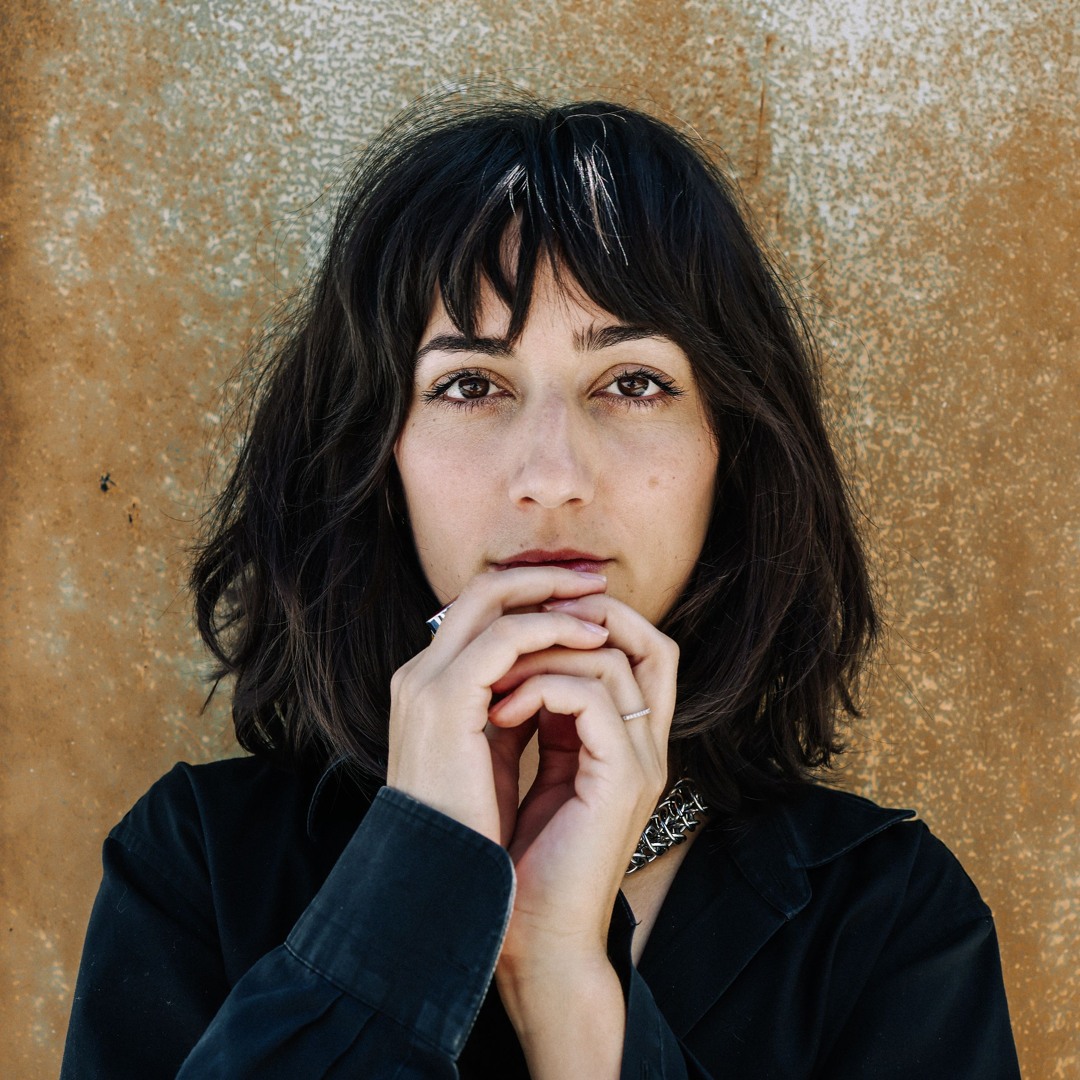 Woman with black bangs resting chin on hands against textured brown wall