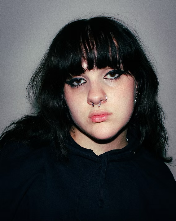 Person with black shoulder-length hair and bangs wearing black hoodie against gray background