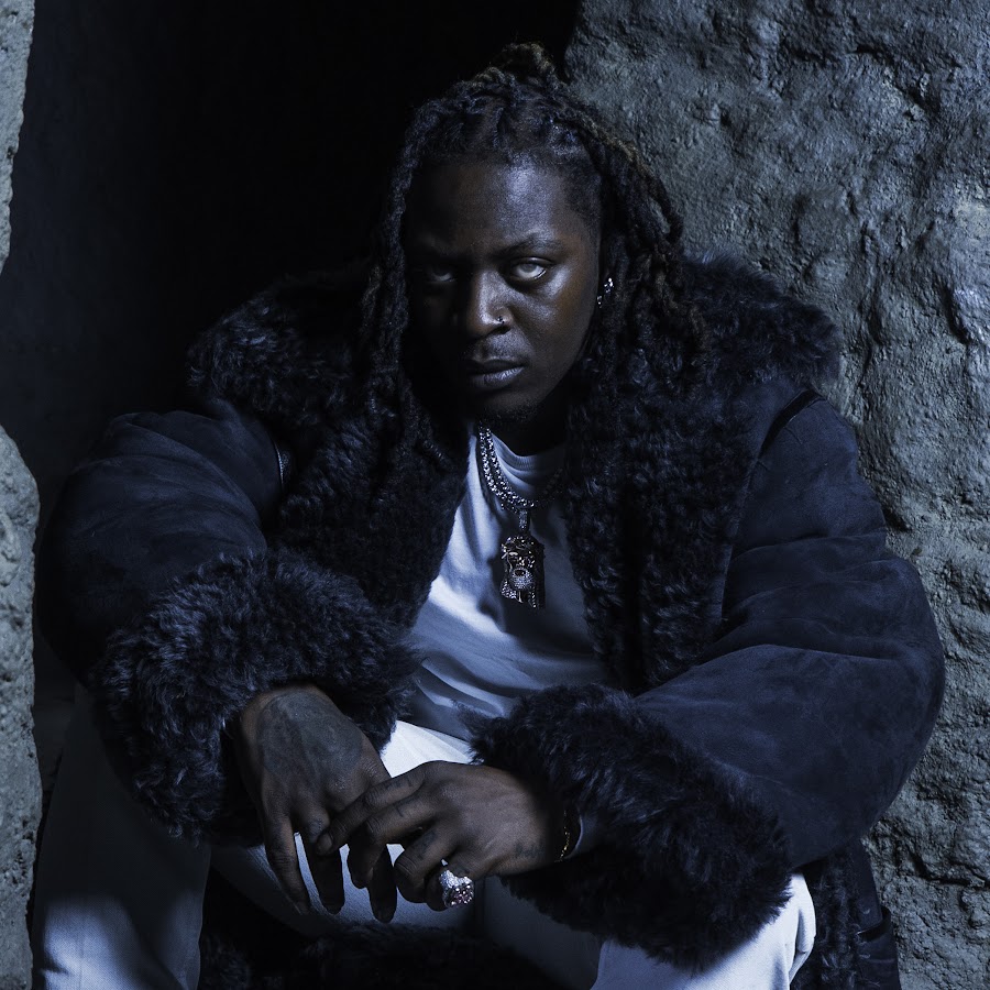 Woman with long braided hair wearing fur-lined jacket against textured stone wall