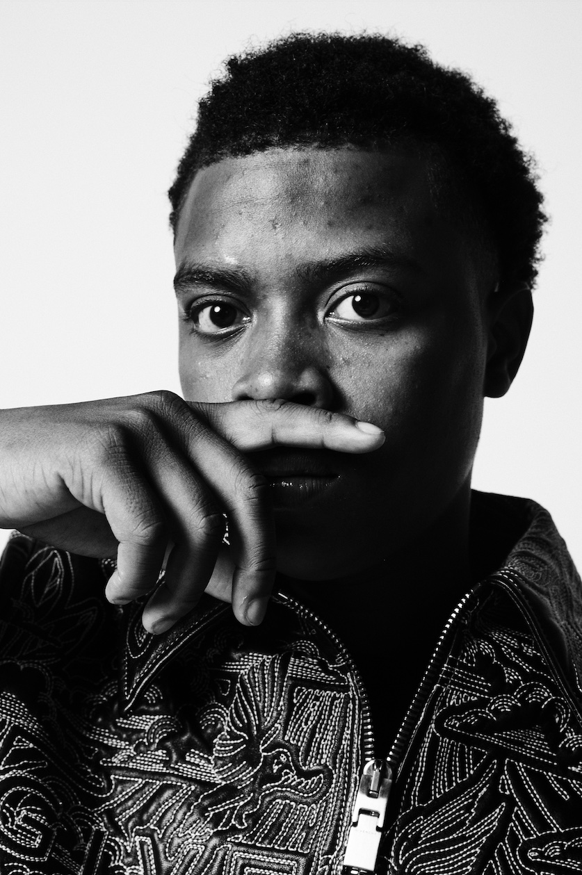 Black and white portrait of man with hand to face wearing patterned shirt