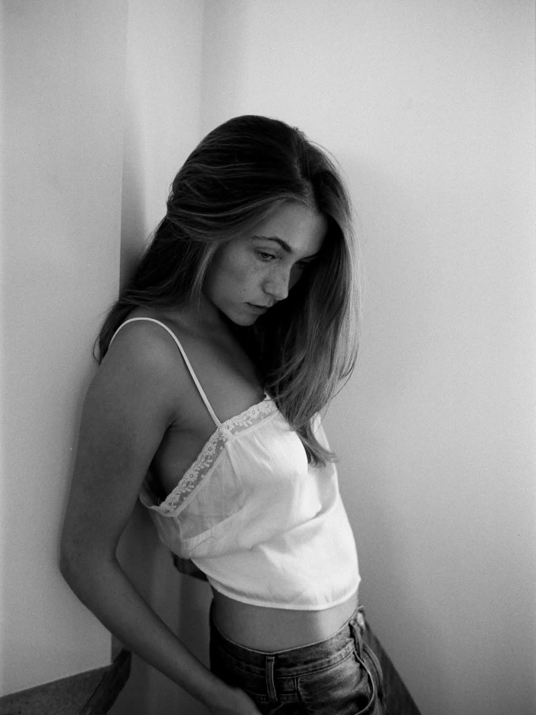 Black and white portrait of woman with long dark hair against white wall, looking down pensively