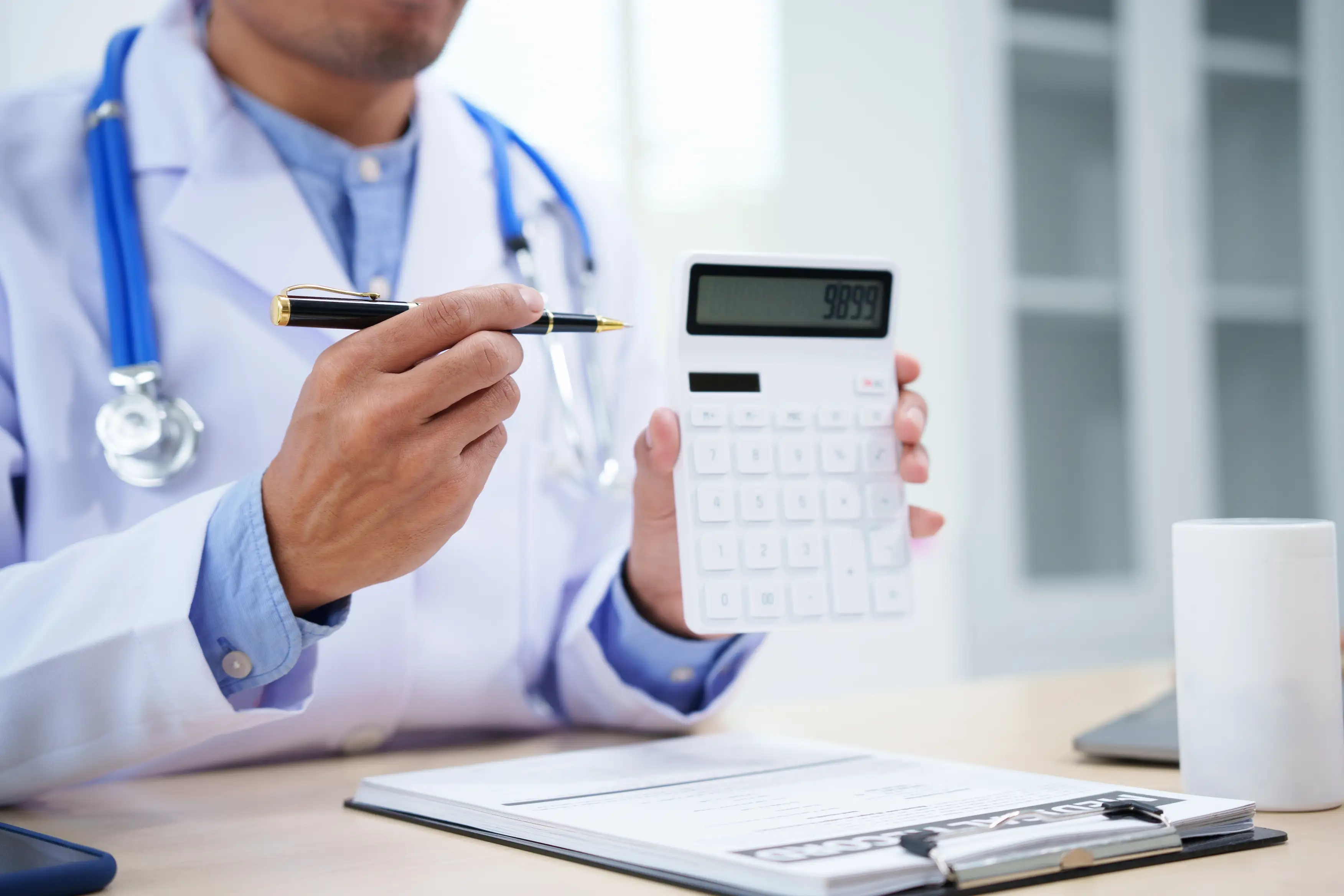 medical doctor is working at a desk, holding a calculator, analyzing patient data related to heart attacks and calculating medical costs to ensure accurate billing and financial management
