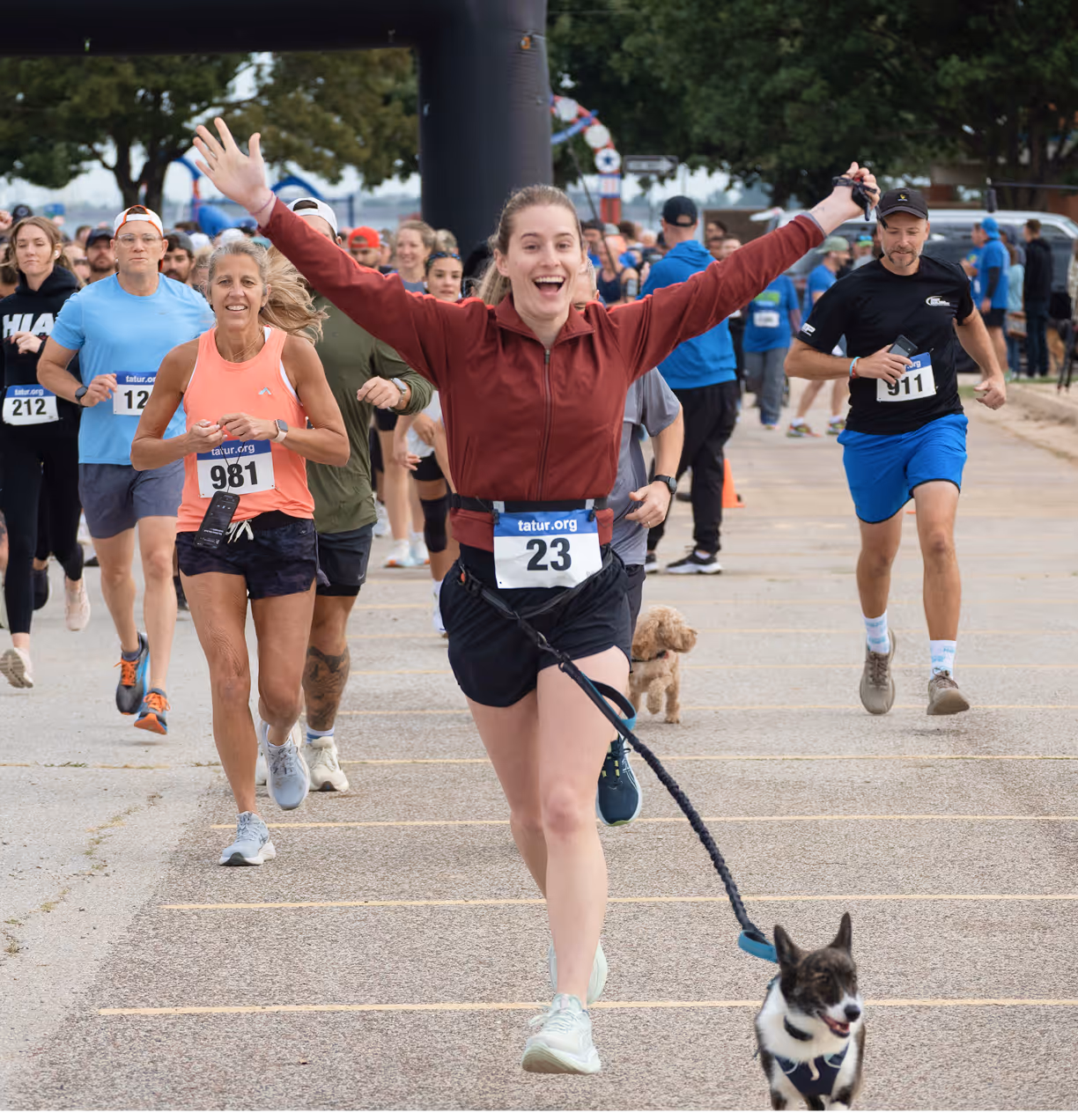 Smiling woman in a maroon jacket running with a dog on a leash toward the camera during the run for hope with other runners behind her.