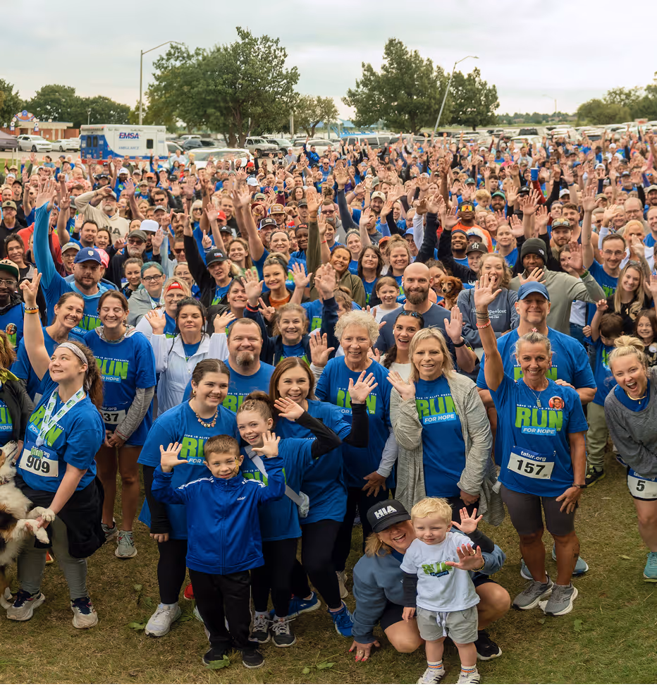 Large group of people wearing blue 'Run for Hope' shirts gathered outdoors, smiling and waving at the camera.