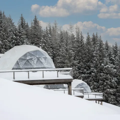 Vue extérieure de dômes Whitepod enneigés dans les Alpes, représentant une destination hôtelière durable imaginée par Momerable.