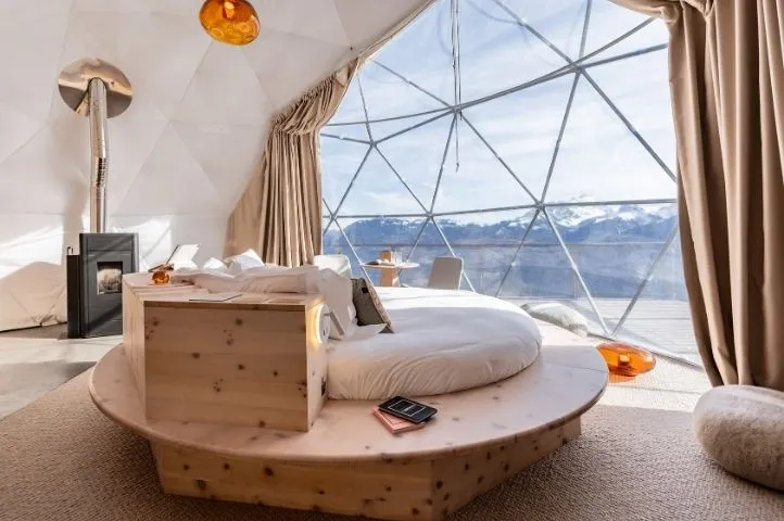 Photo d’un lit rond au centre d’un dôme Whitepod, illustrant le design intérieur unique et l’expérience immersive pensée par Momerable.