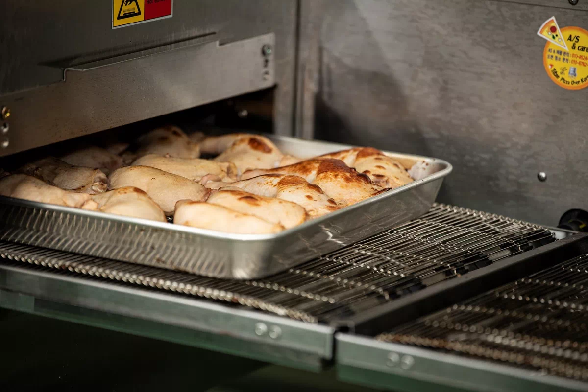 구운 닭다리 여러 개가 금속 쟁반에 담겨 오븐에서 나오고 있는 모습.