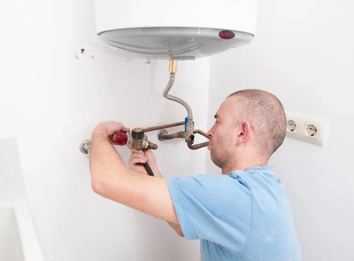 A plumber working on replacing a water heater system using a tool
