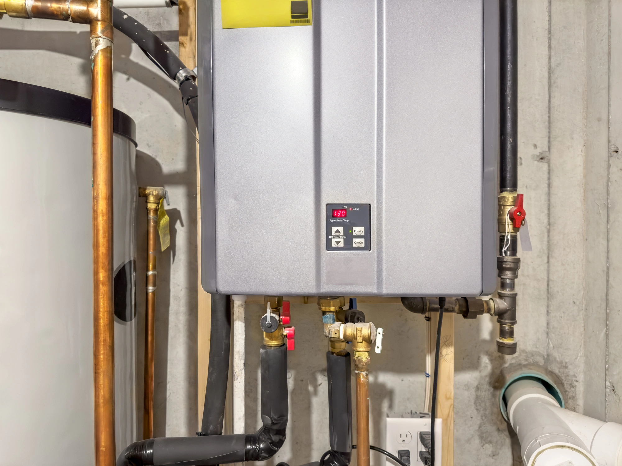 A modern tankless water heater installed on a concrete wall, displaying a temperature readout of 130°F.