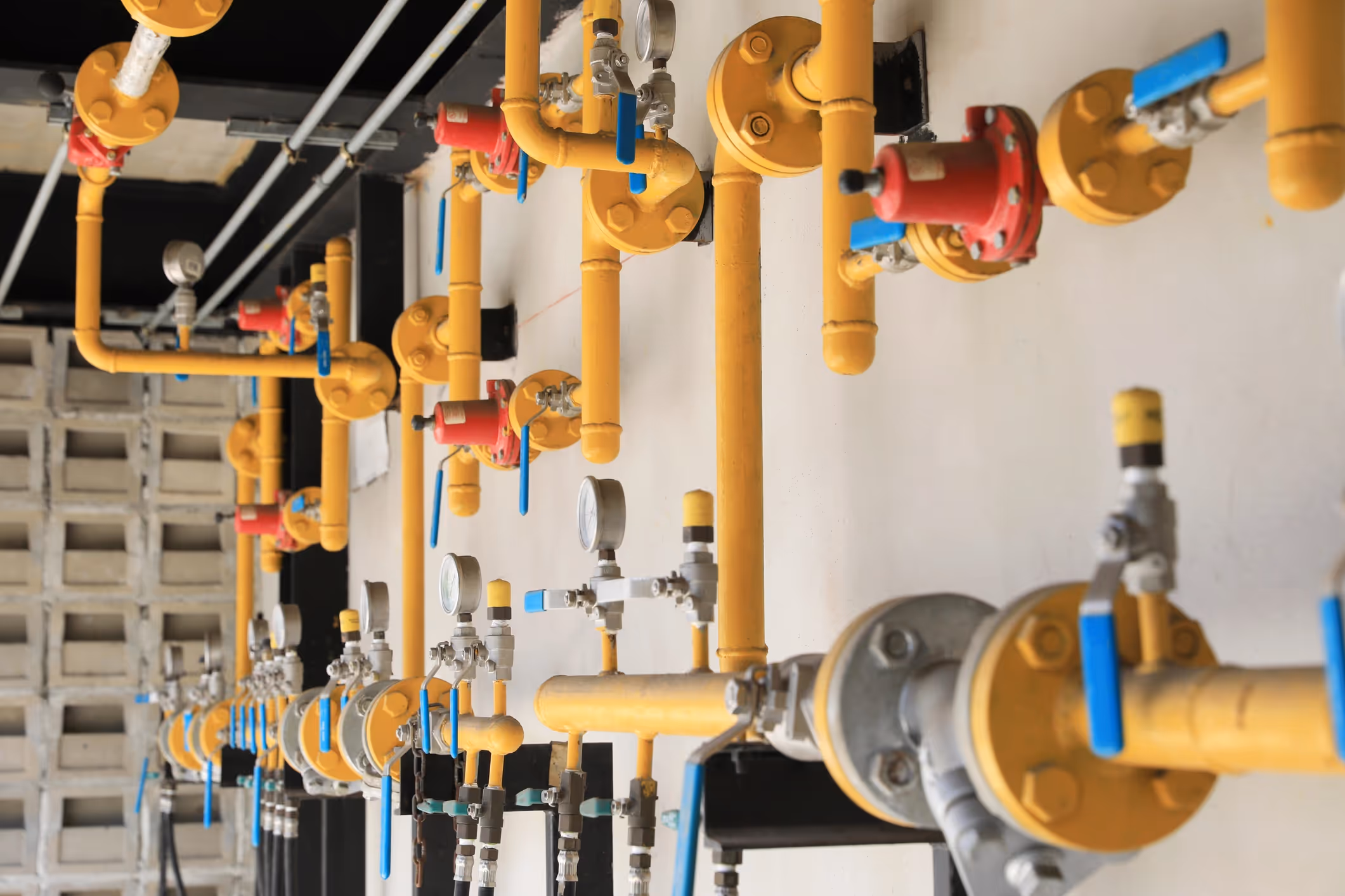 Industrial setup with yellow gas pipes and blue valves against a white wall.