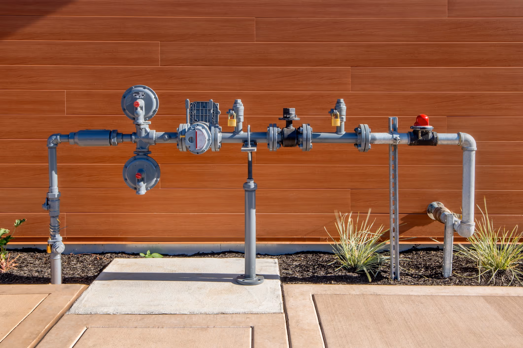 Outdoor gas meter and pipe system against a brown wooden wall. 