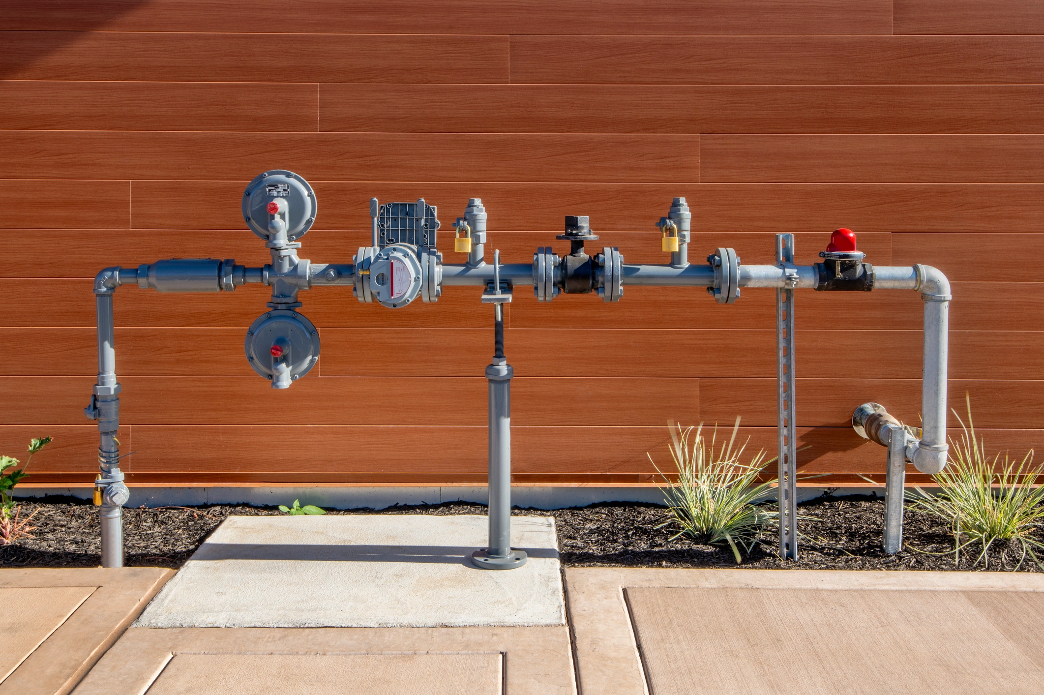 Outdoor gas meter and pipe system against a brown wooden wall. 