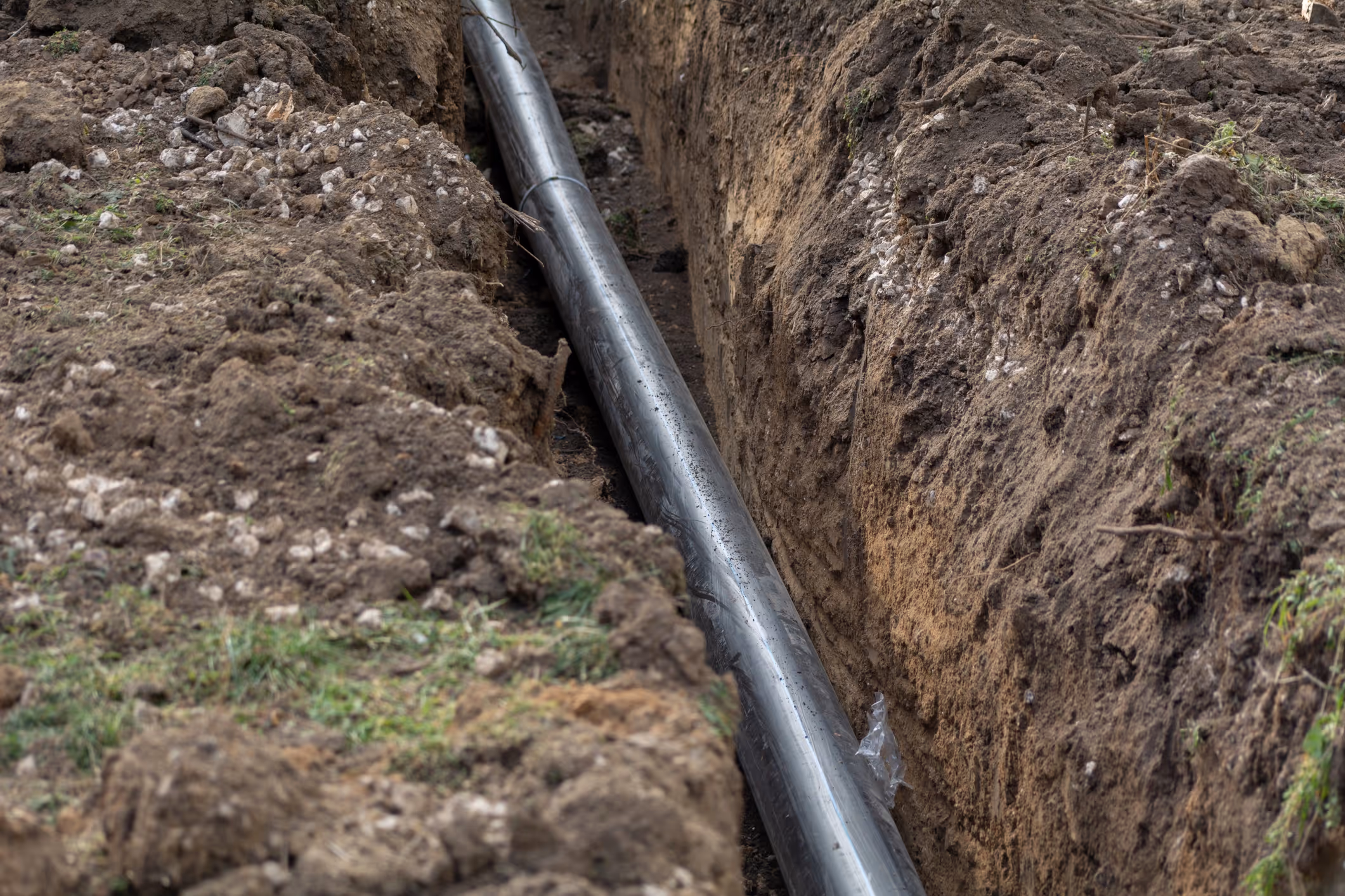 A black pipe runs through a narrow trench dug in the earth. 