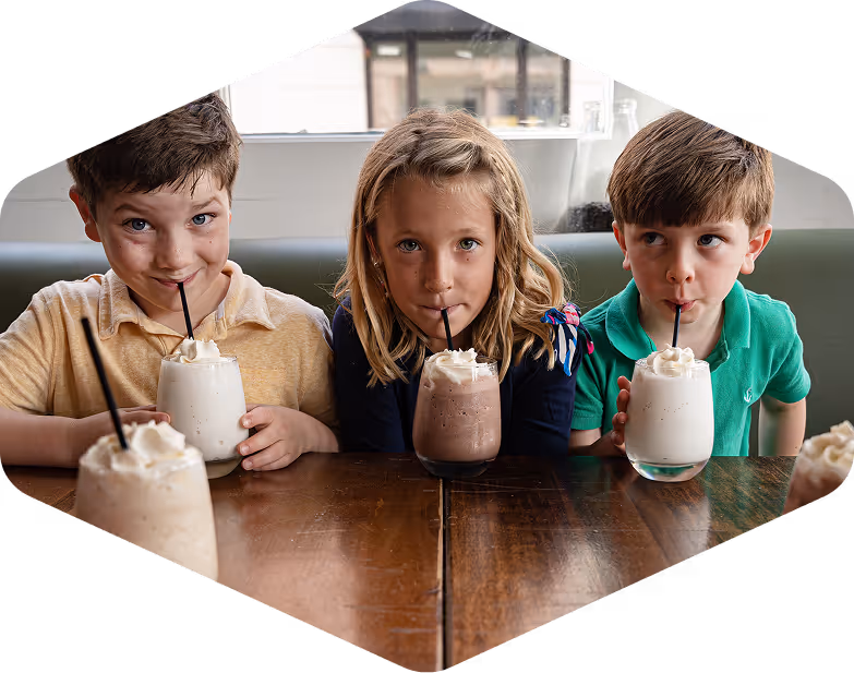 Three happy children drinking milkshakes at Carmella's Bakery
