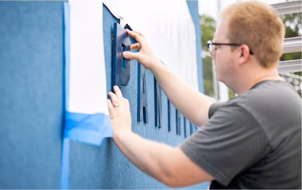 Print technician applying lettering to a blue wall