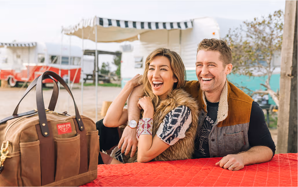 Happy young man and woman sitting at a table with a travel bag displayed