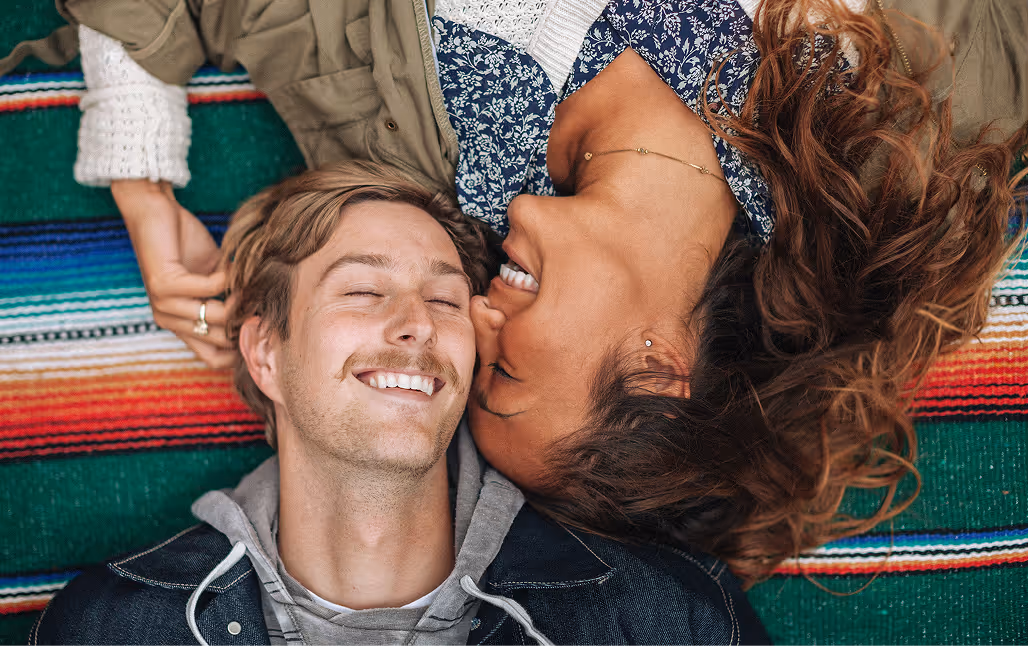 Overhead angle of a smiling young man and woman laying together on a beach blanket