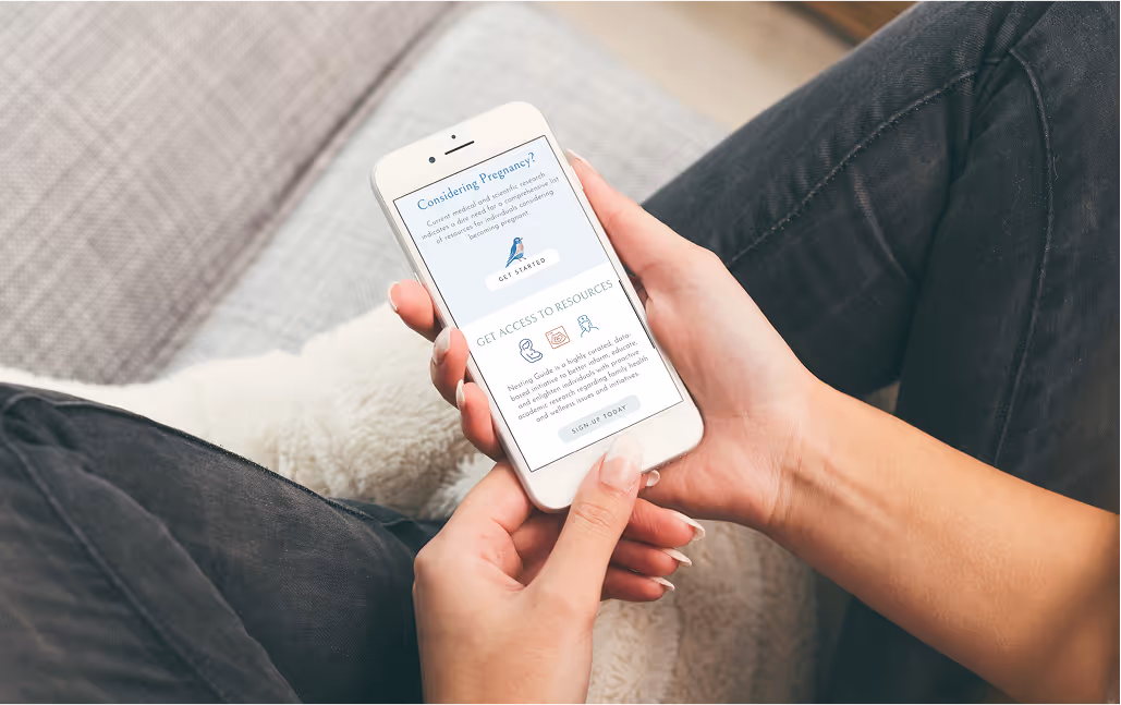 Overhead angle of a woman's hands holding a smartphone displaying a website featuring pregnancy information