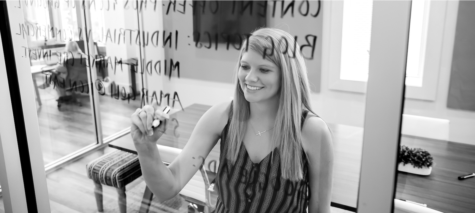 Woman writing marketing strategy notes on a glass wall in an office, brainstorming content creation ideas.