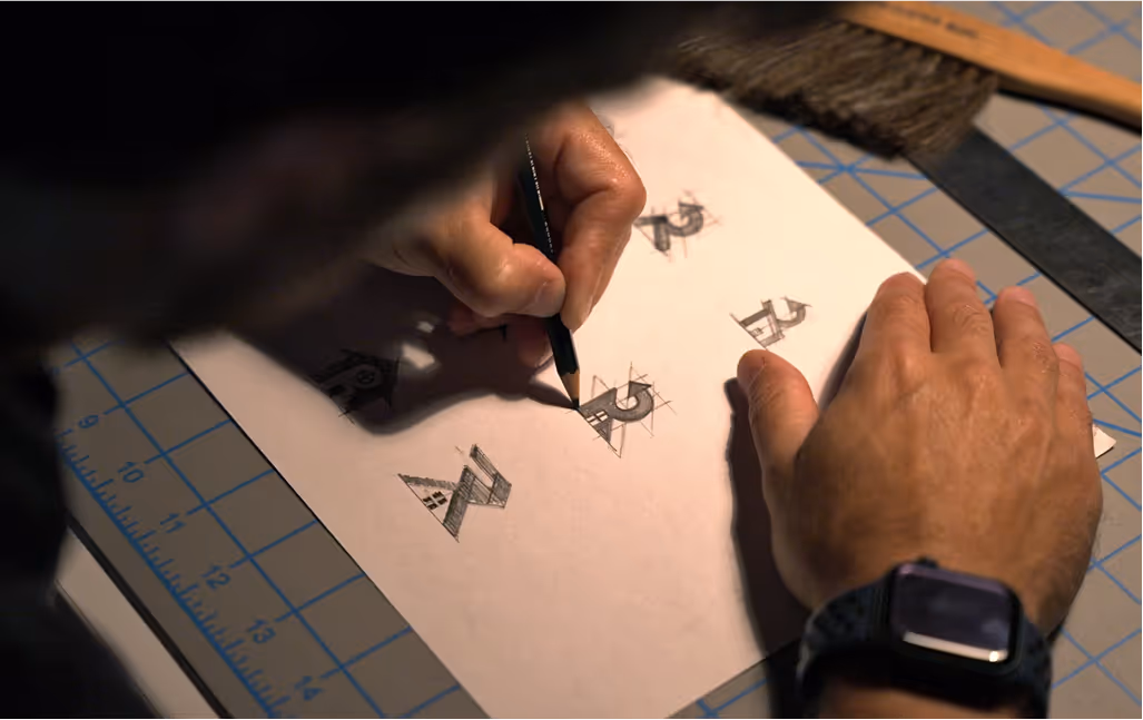 Close-up of designer sketching Restorify logo concepts with pencil on paper over a grid-lined cutting mat
