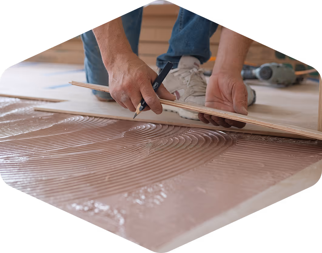 Contractor marking and installing hardwood flooring with adhesive during a professional floor installation project.