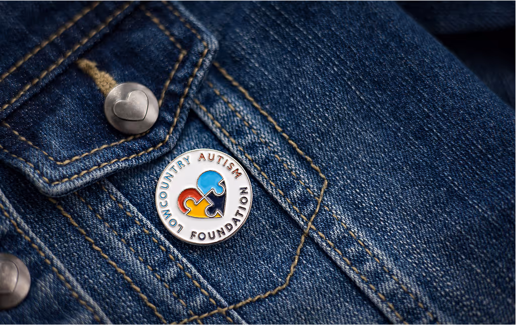 Close up image of a Low Country Autism pin attached to a denim jacket pocket