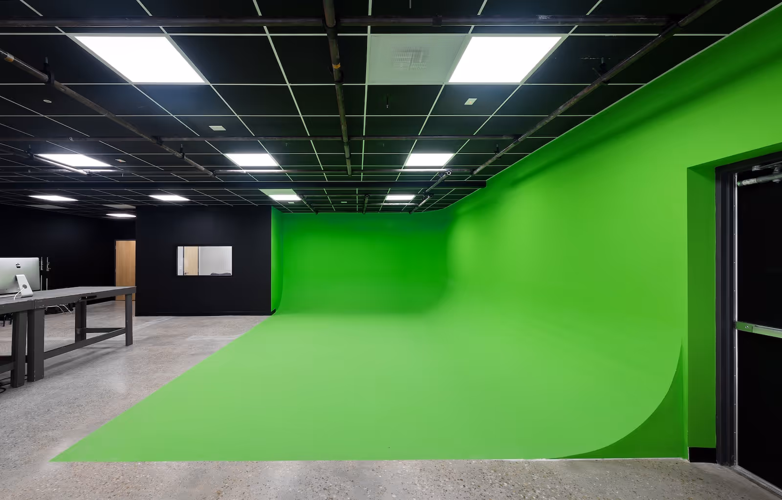 Front-facing view of large seamless green screen wall with curved cyc floor and ceiling-mounted lights in Rift Studios.