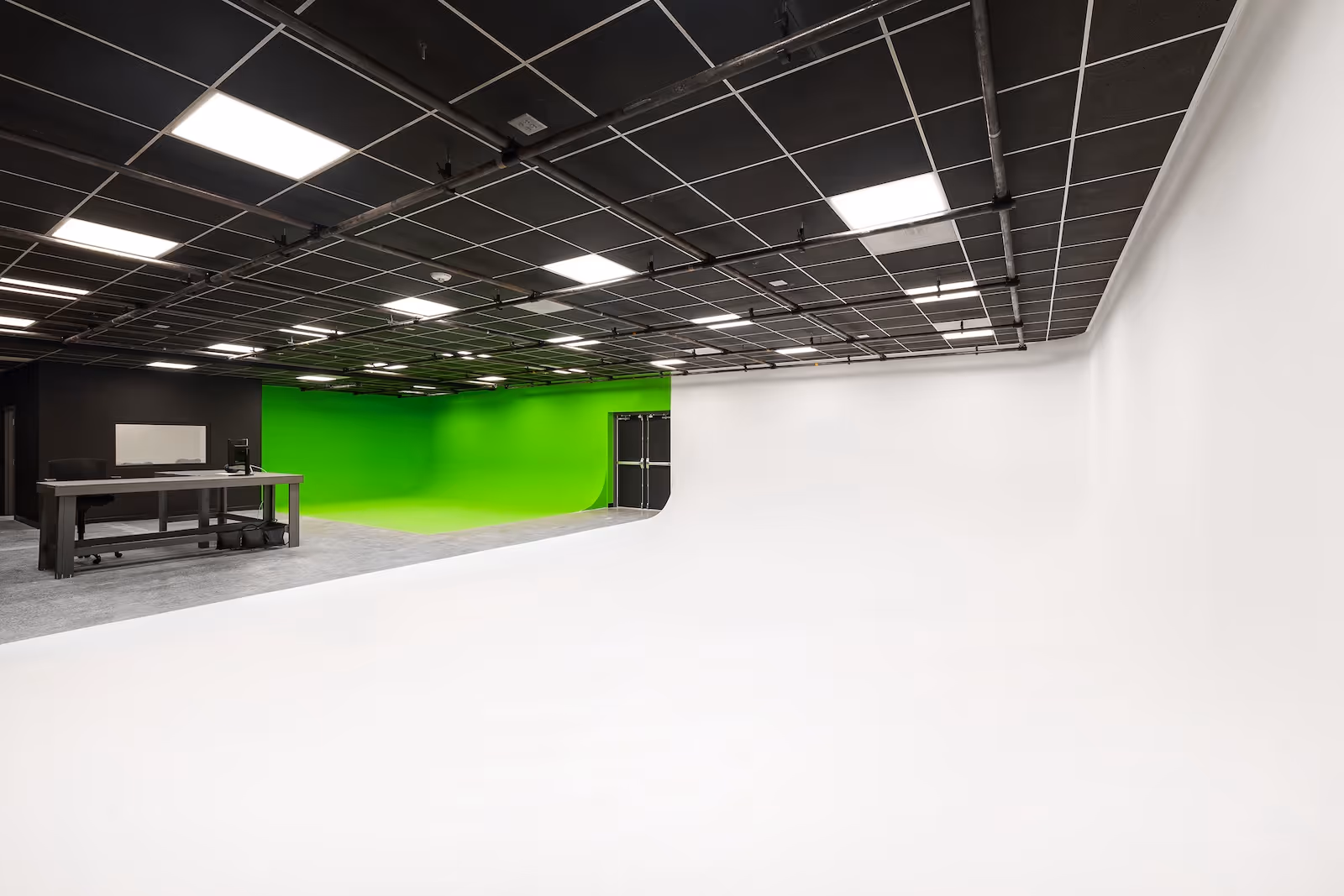 Modern video production studio with white and green cyc walls, black grid ceiling, and editing workstation at Rift Studios.