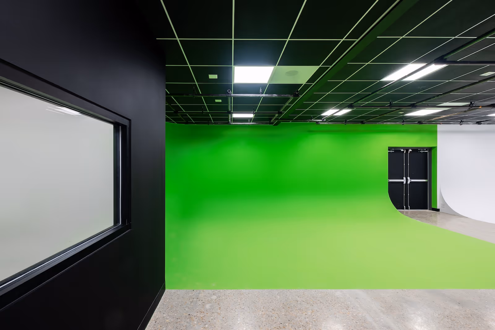 Side view of Rift Studios’ green cyc wall and double door exit, with concrete floor and soundproof black wall with window.