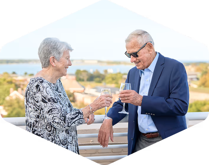 Happy senior couple clinking wine glasses on rooftop balcony with scenic view, representing vibrant retirement lifestyle