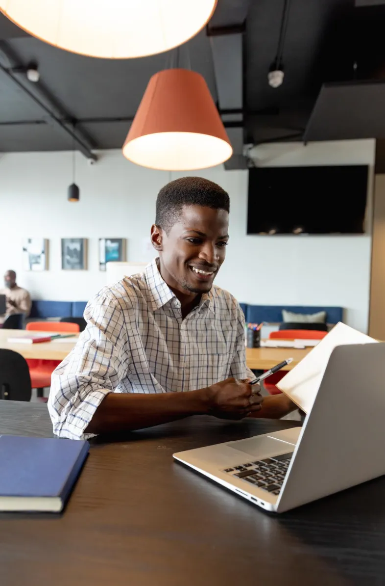 Man smiling at a laptop in a modern workspace.