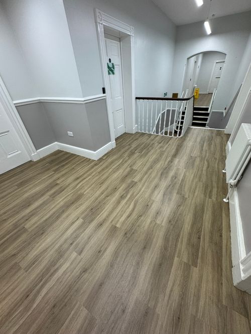 Interior hallway with light wood flooring, white and gray walls, white doors, white banister around staircase, a radiator on the right wall, and fluorescent ceiling lights.