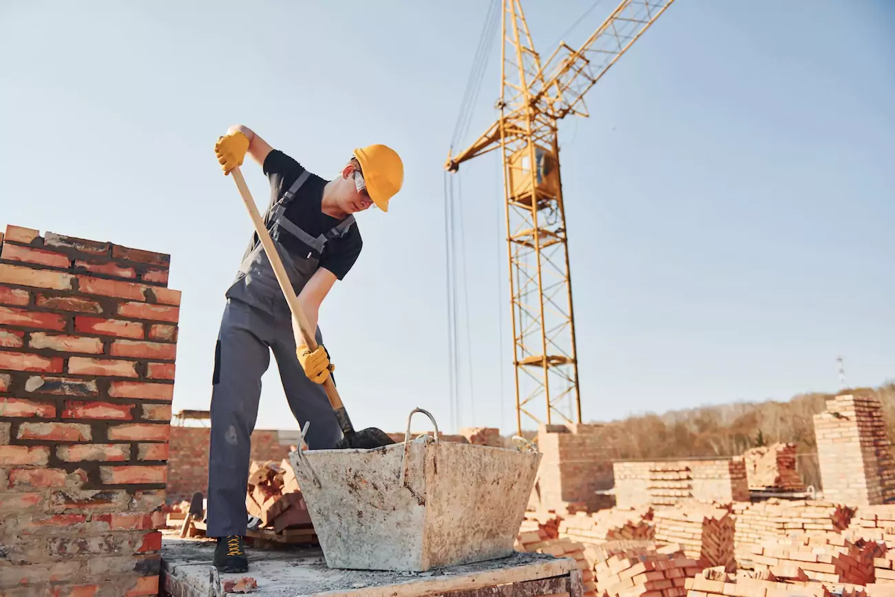 Builder removing ground waste with a shovel.