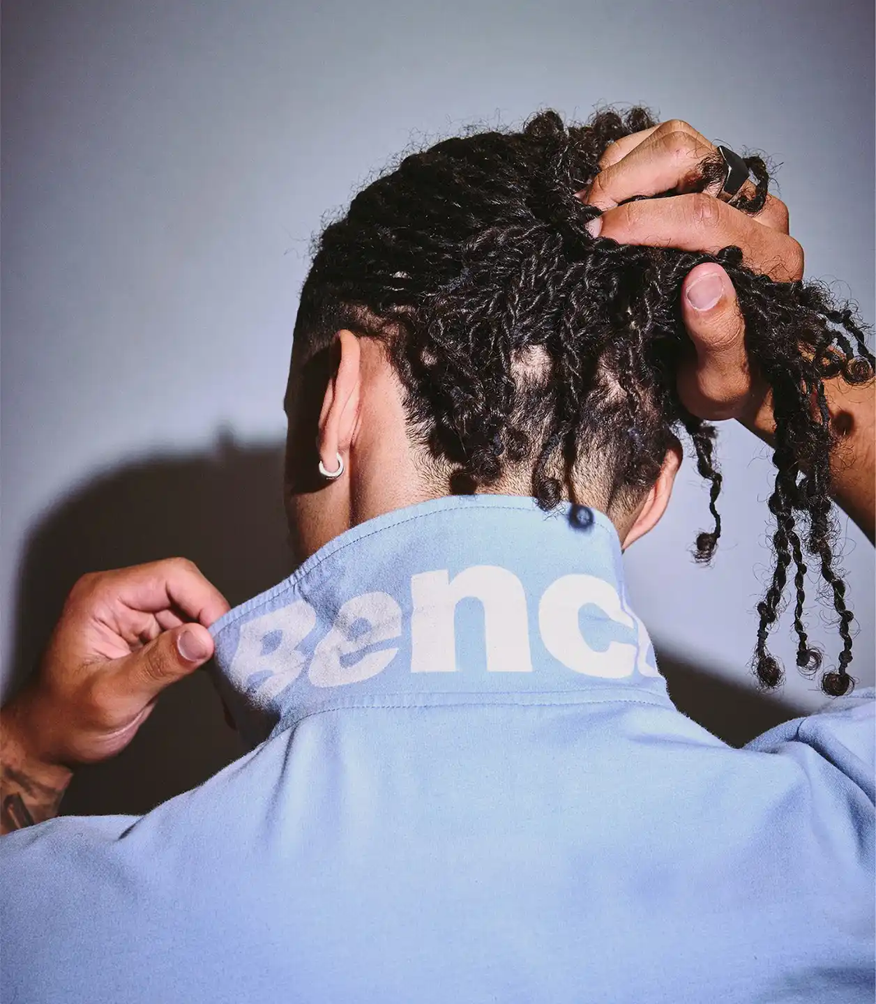 An image of a man Holding Curly Black Hair and a blue Top