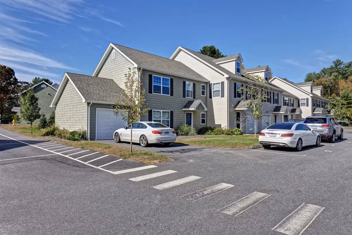 Residential street scene showing modern townhome apartment buildings with individual garages and parked cars, at Meadowbrook Gardens in Mansfield Center, CT.