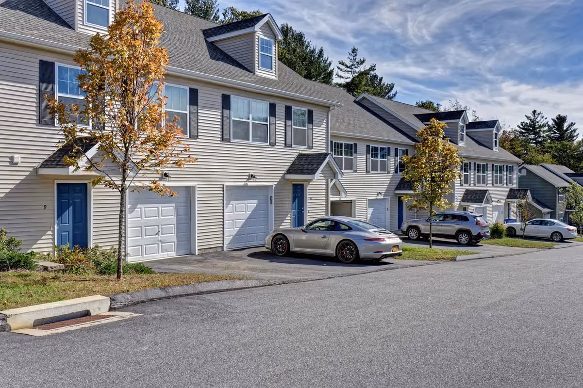 Front view of townhome apartment units with individual garages and driveways, offering convenient parking at Meadowbrook Gardens in Mansfield Center, CT.