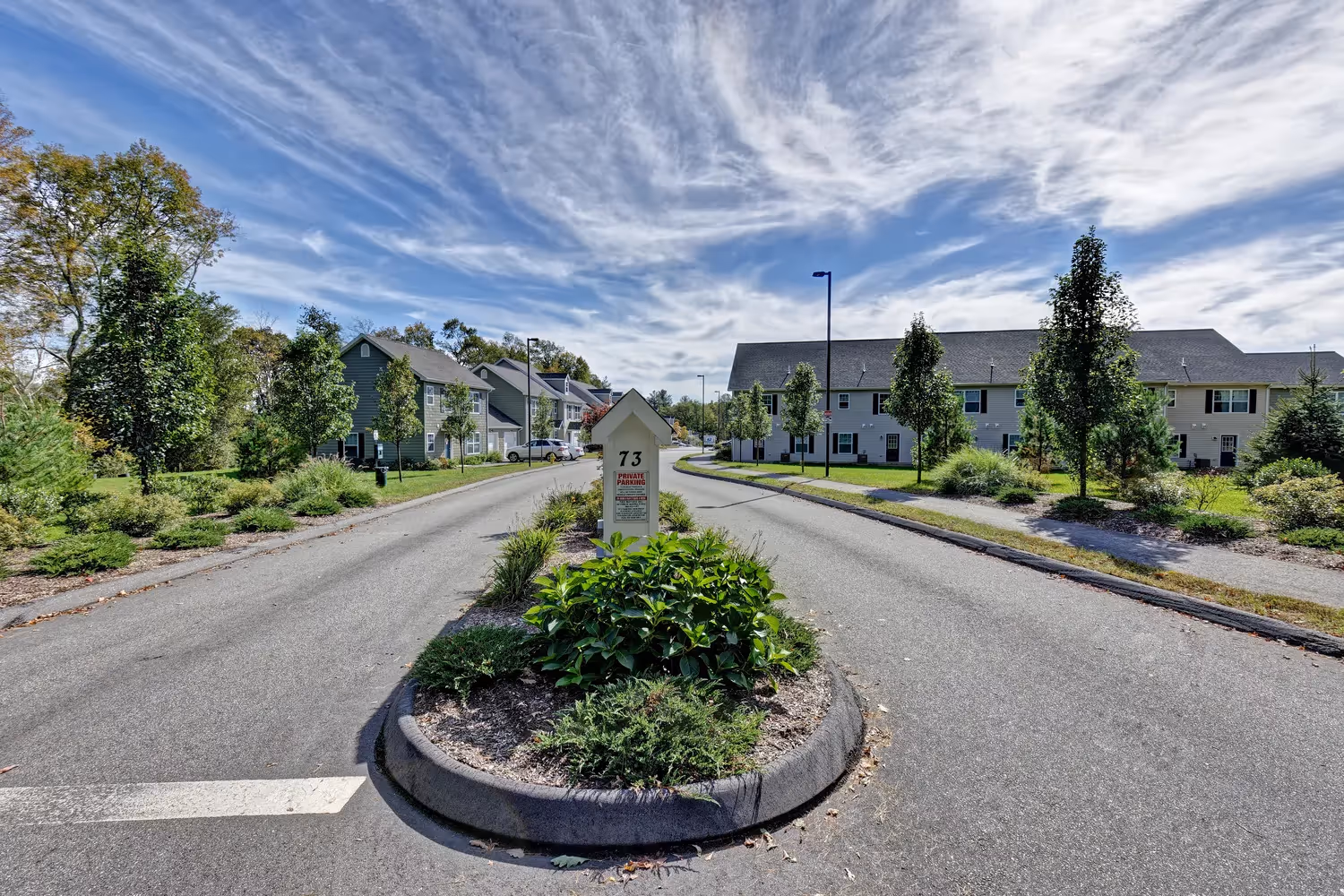 Entrance road to Meadowbrook Gardens apartment community in Mansfield Center, CT, surrounded by landscaping and residential buildings.