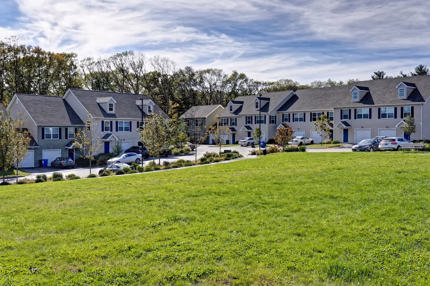 Row of charming townhome-style apartment buildings with blue doors, set on a green hillside at Meadowbrook Gardens in Mansfield Center, CT.