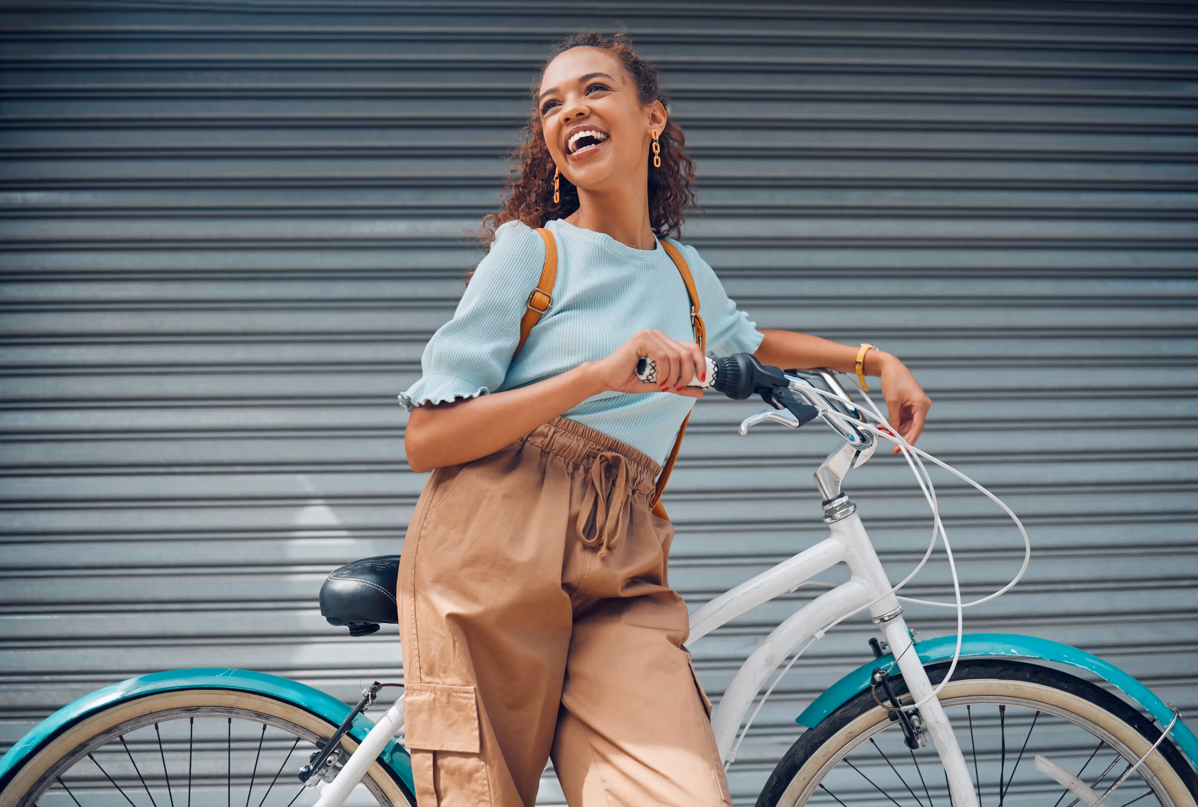 Young woman smiling while walking her bike near Meadowbrook Gardens apartments in Mansfield, CT, embracing an active and vibrant lifestyle